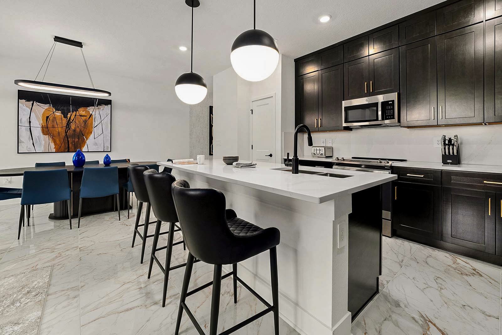 A contemporary kitchen featuring dark cabinetry, white quartz countertops, a large island with black leather barstools, and an adjoining dining table.