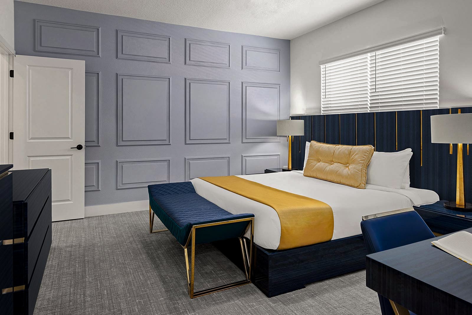 A spacious master bedroom featuring a blue paneled accent wall, a king bed with gold accents, and a matching upholstered bench at the foot of the bed.