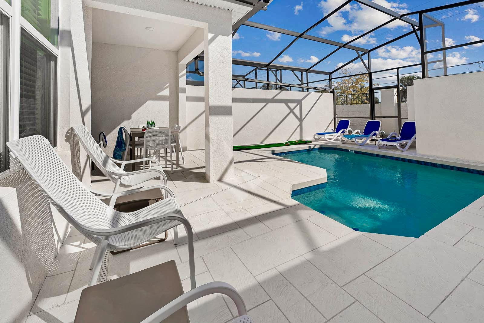 A sunlit private patio enclosed by a screen, featuring a small swimming pool, lounge chairs, and an outdoor dining area.