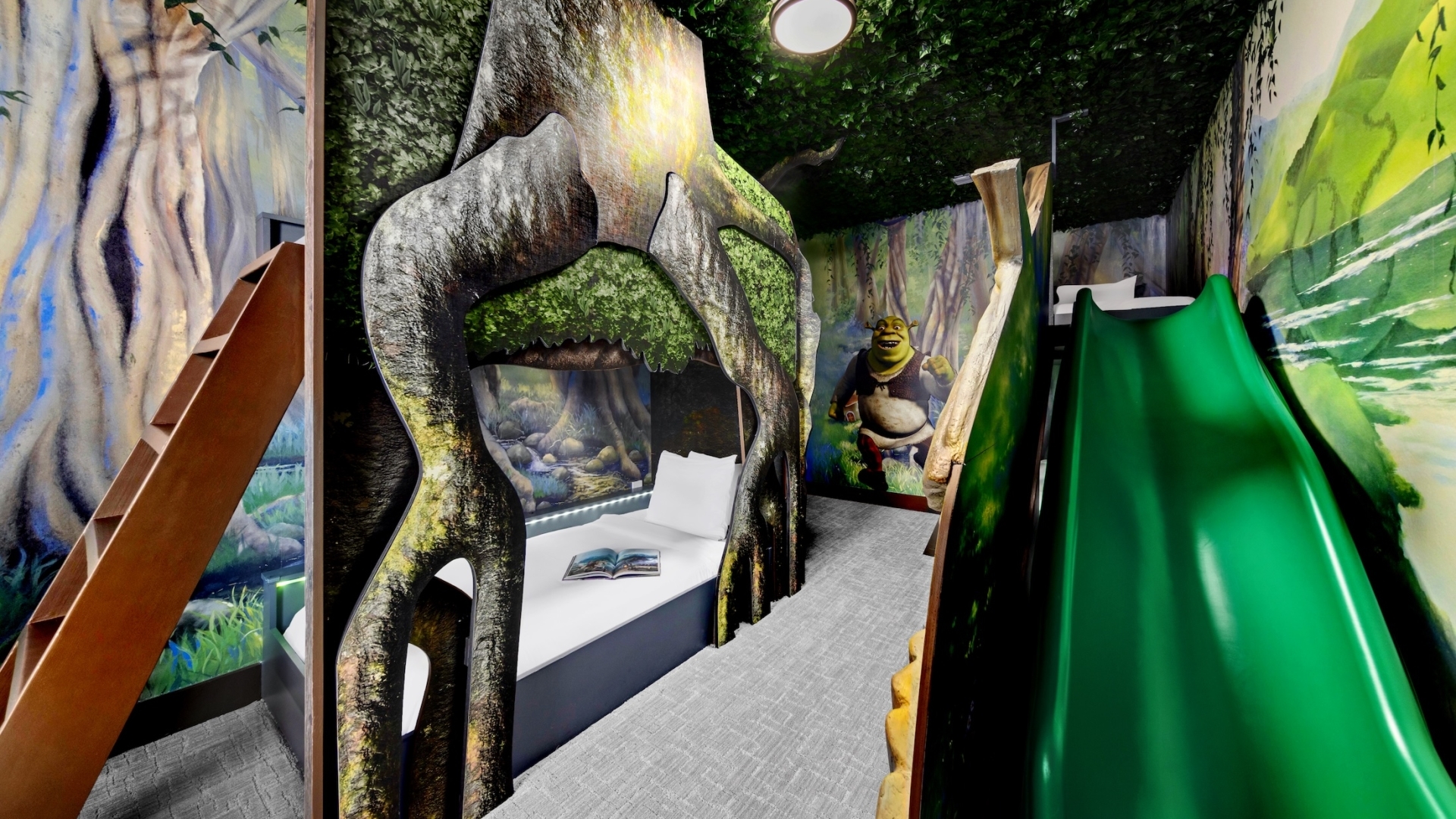 A swamp-themed children's bedroom featuring a tree-root-shaped bunk bed, a green slide, a faux-leaf ceiling, and a mural of a popular green ogre character.