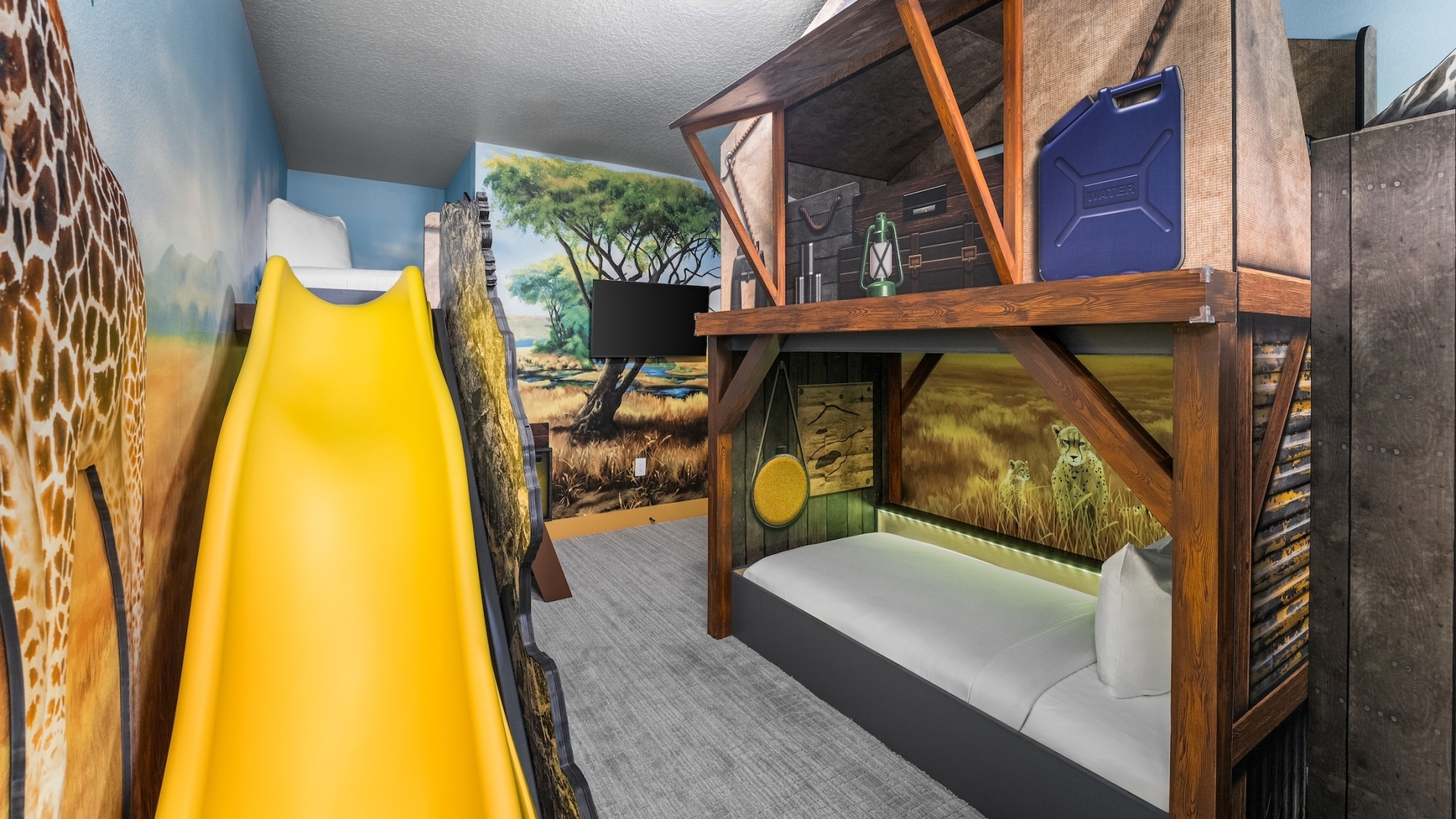 A safari-themed children's bedroom featuring a tent-style bunk bed with wooden framing, a bright yellow slide, and immersive wall murals of a savanna with giraffes and cheetahs.