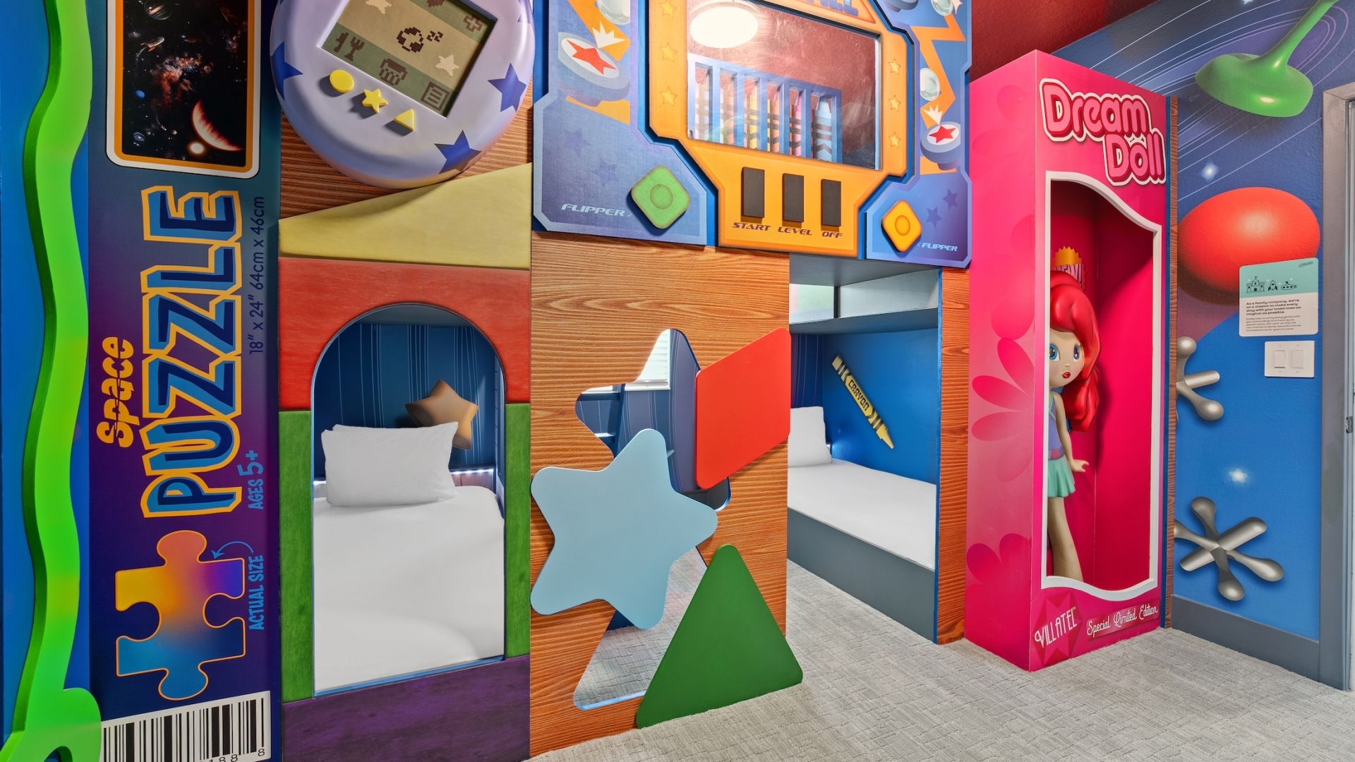 A colorful toy-themed children's bedroom featuring bunk beds built into oversized game boxes, including a pinball machine, digital pet, and space puzzle, alongside a life-sized doll box.