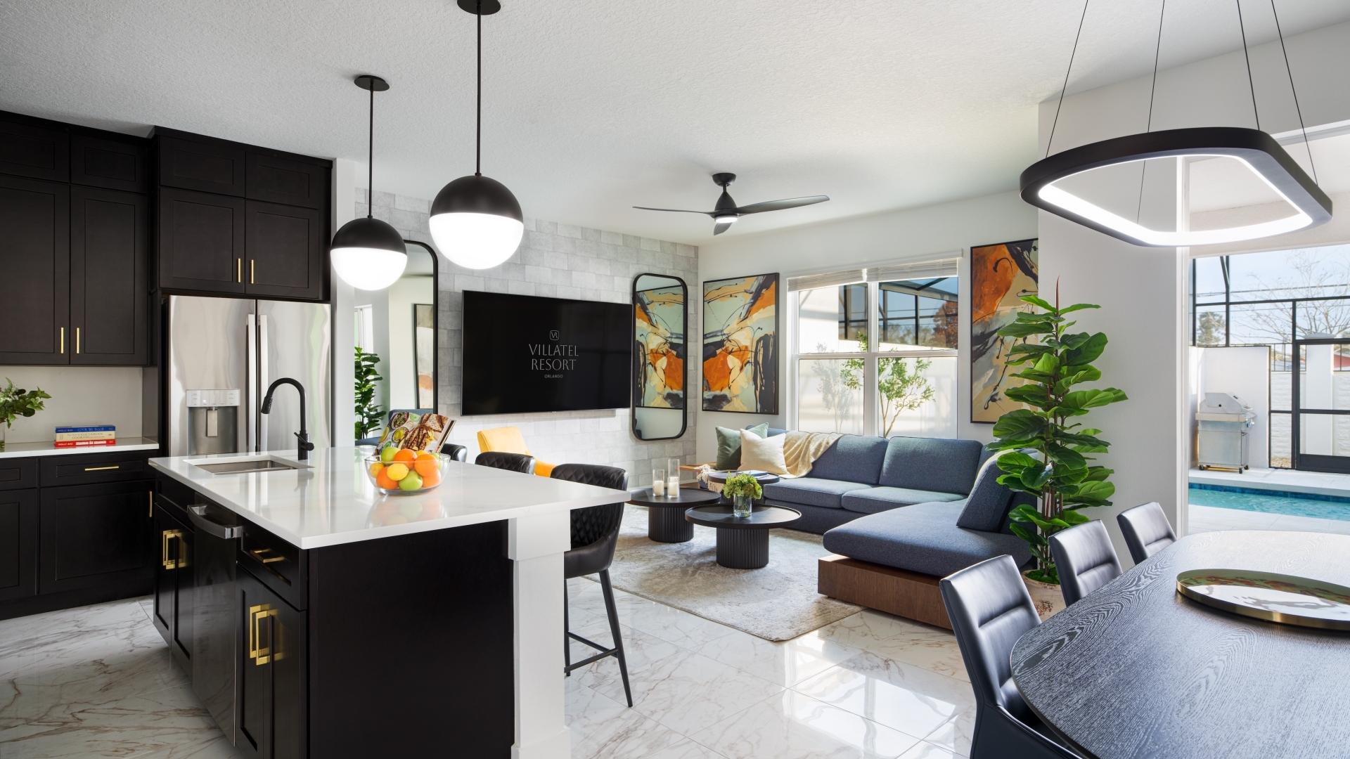 An open-concept villa interior showcasing a sleek kitchen island, a dining table, and a living area with a blue sectional sofa that opens up to a private pool courtyard.