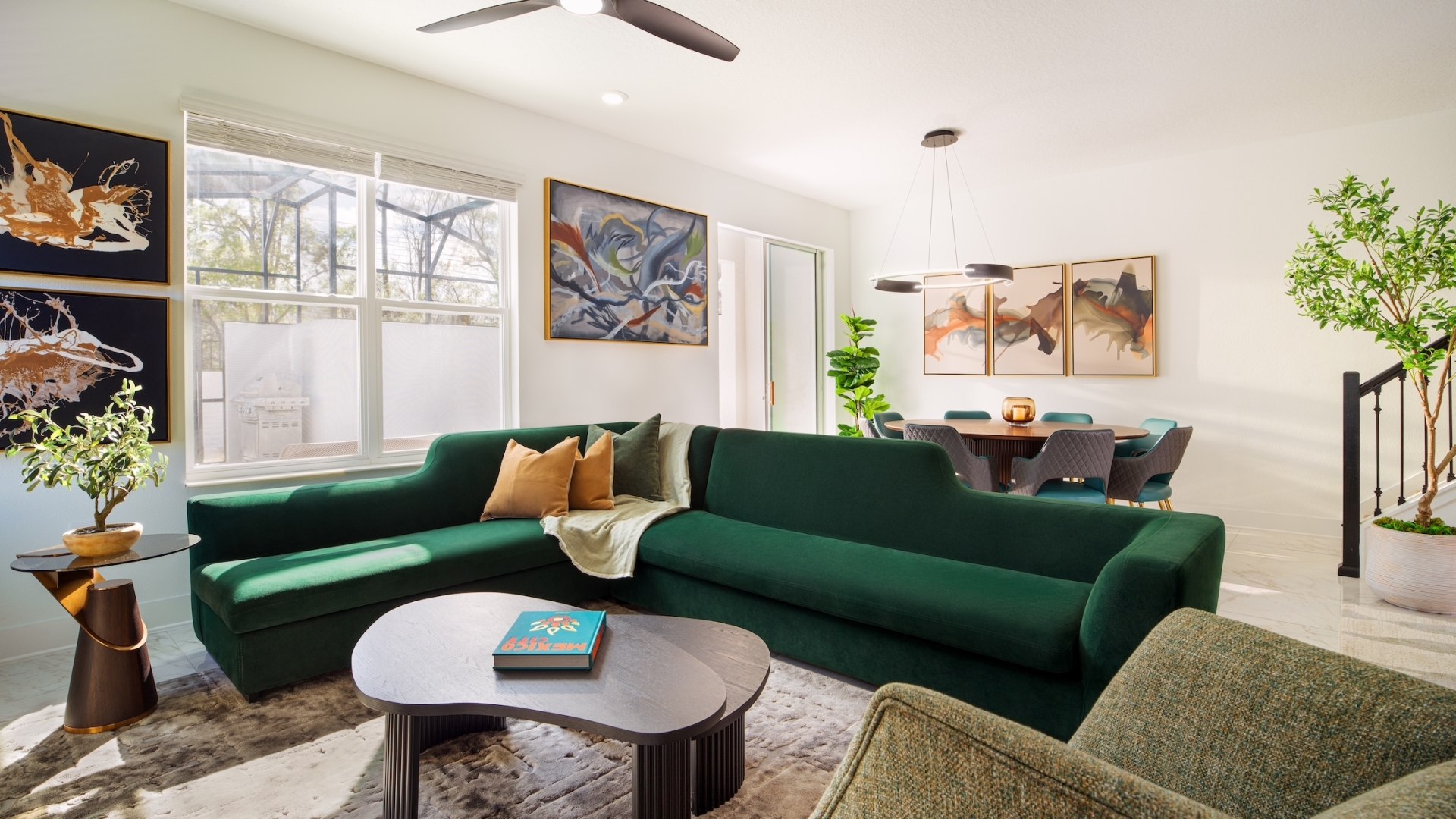 An open-concept living space showcasing a large forest green sectional sofa, abstract wall art, and an adjacent dining area.