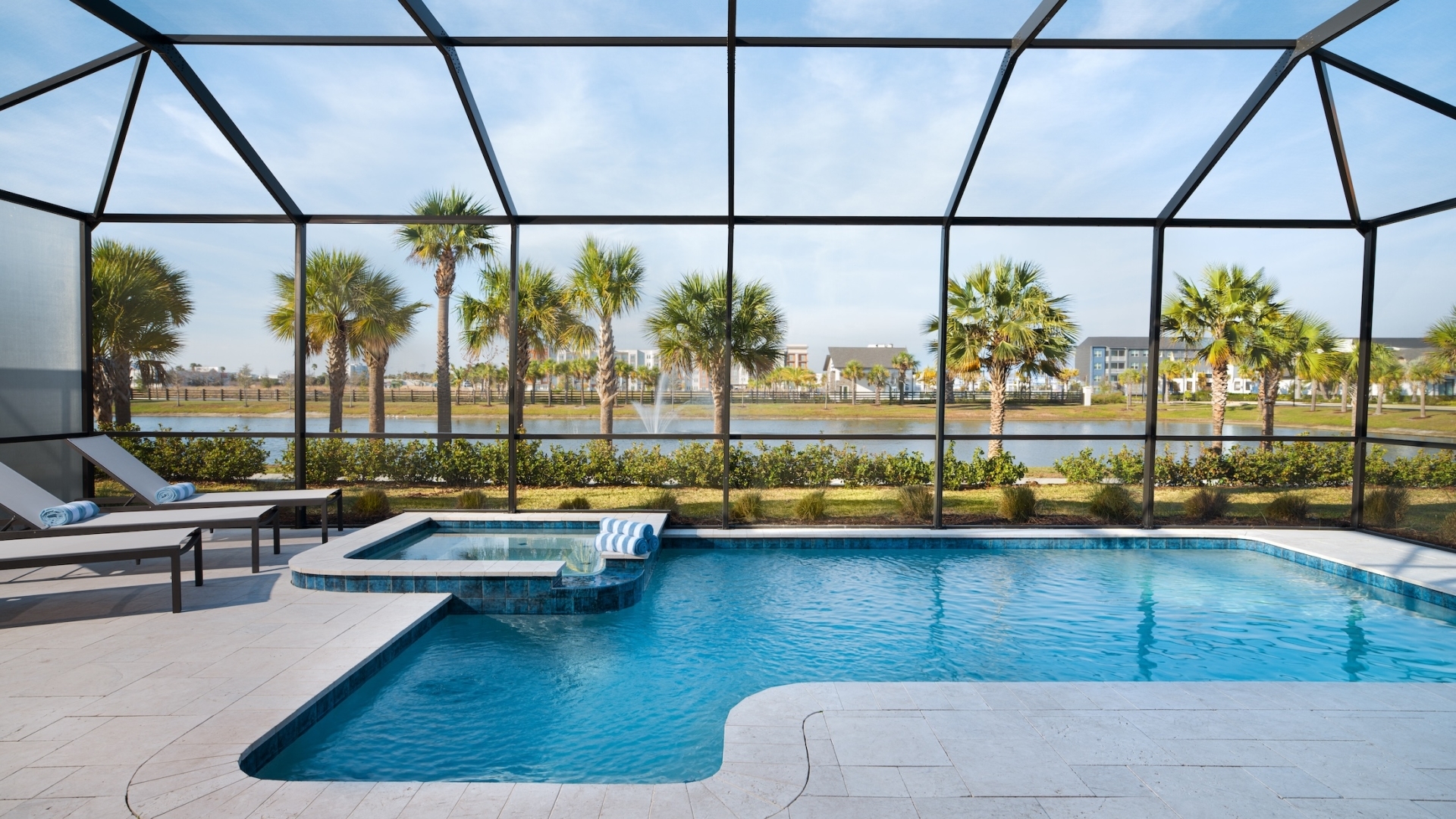 A private screened-in patio area featuring a swimming pool, integrated hot tub, and lounge chairs overlooking a palm tree-lined resort lake.