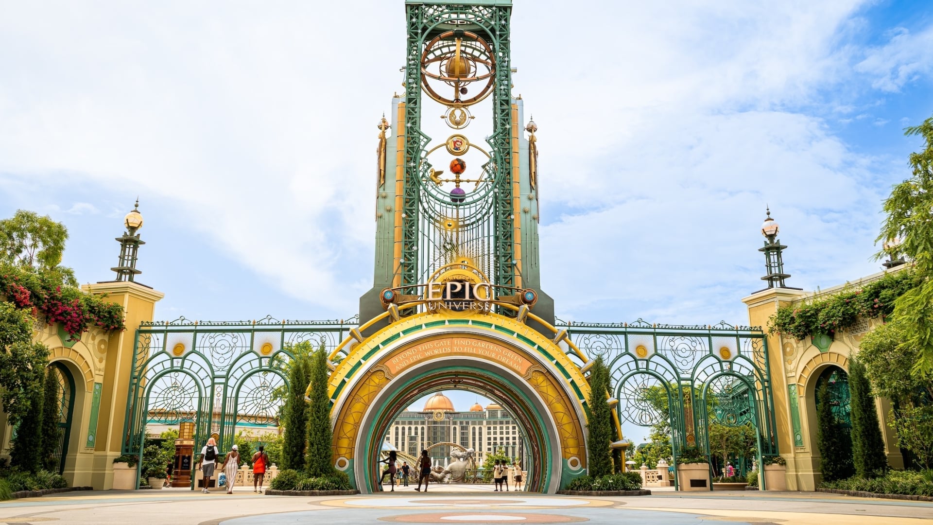 The grand entrance portal of Universal Epic Universe, featuring a tall green celestial-themed clock tower and ornate iron gates.