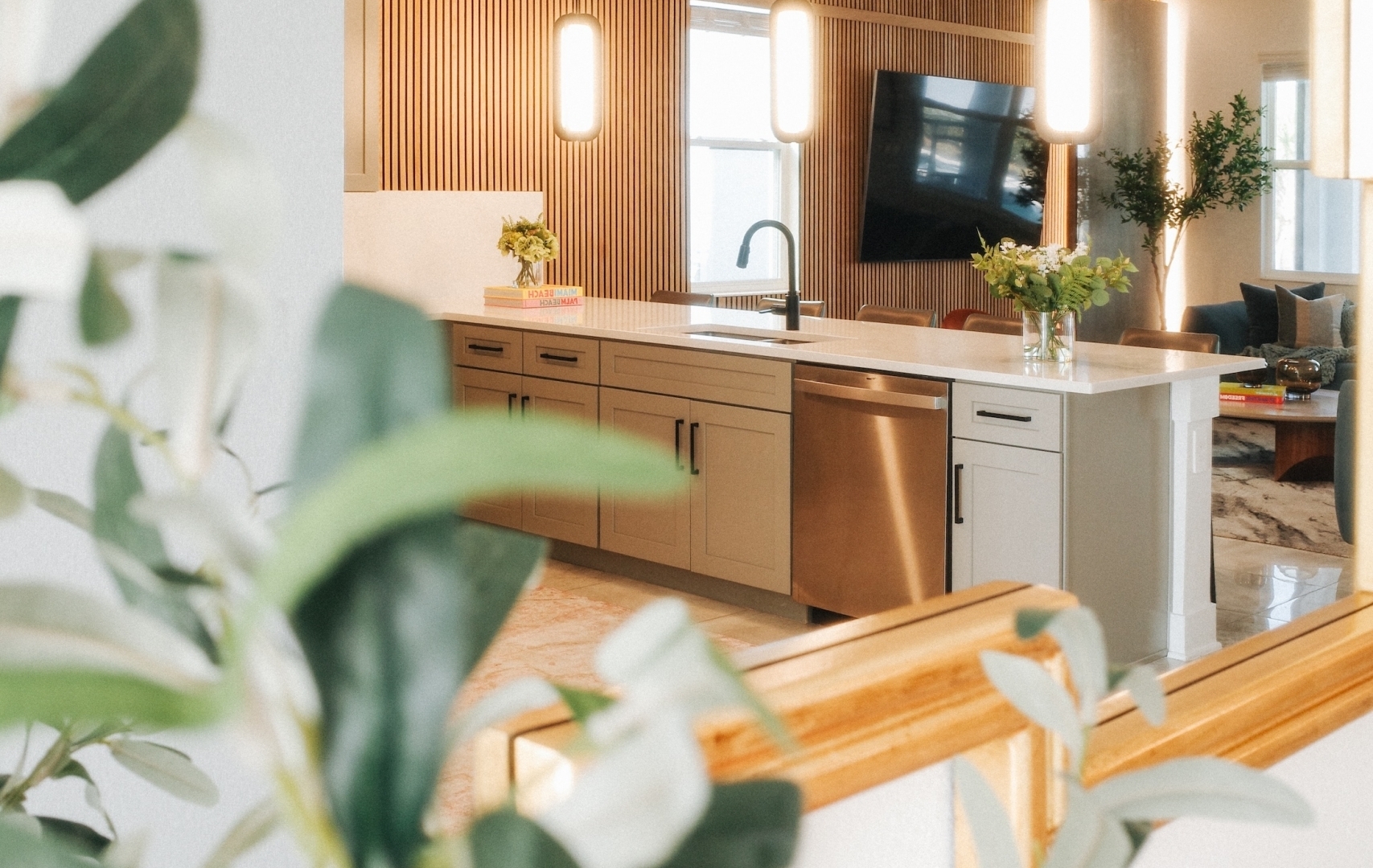 A view from a foyer looking into a modern open-concept kitchen featuring an island, wooden slat wall accents, and warm pendant lighting.